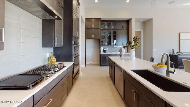 kitchen with dark brown cabinetry, sink, wall chimney exhaust hood, stainless steel appliances, and tasteful backsplash