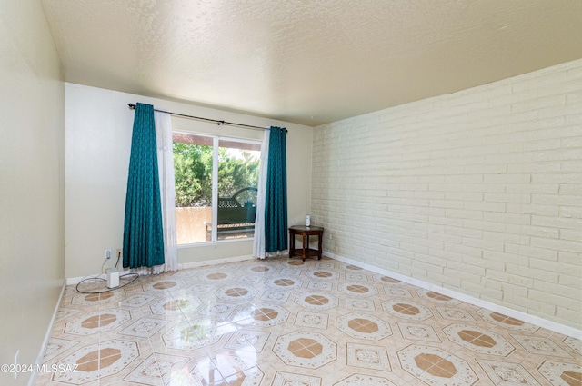 unfurnished room featuring brick wall and a textured ceiling