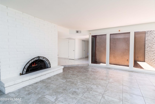 unfurnished living room featuring light tile patterned flooring, a brick fireplace, and brick wall