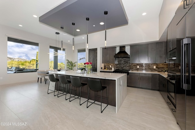 kitchen with a spacious island, wall chimney exhaust hood, a kitchen breakfast bar, pendant lighting, and backsplash