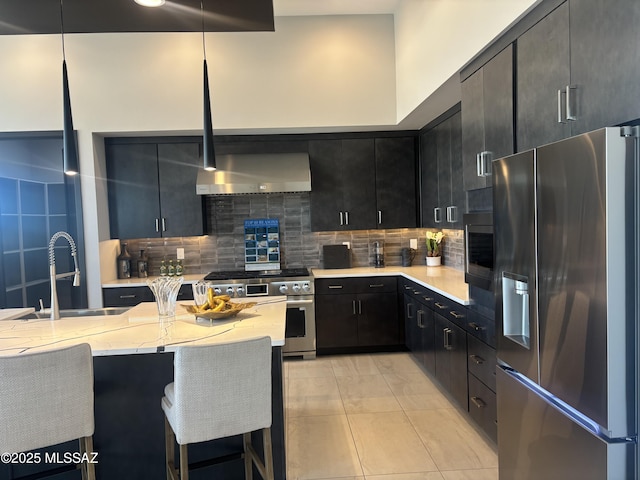 kitchen featuring a sink, decorative backsplash, a breakfast bar area, appliances with stainless steel finishes, and dark cabinets