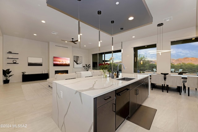 kitchen featuring a large island with sink, sink, pendant lighting, and light stone counters