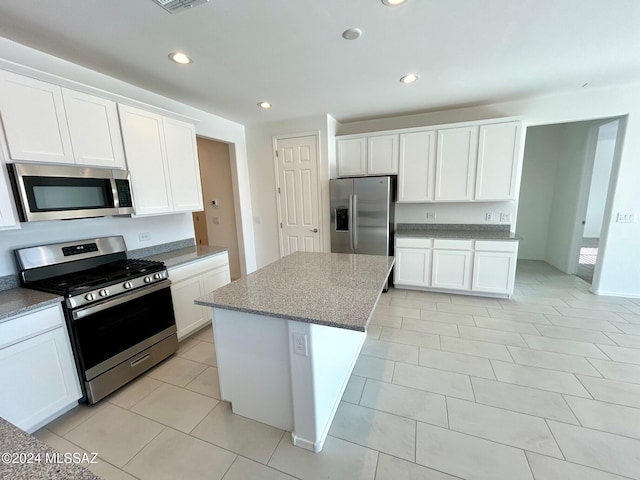 kitchen with light stone countertops, white cabinetry, a center island, stainless steel appliances, and light tile patterned floors