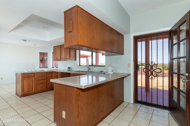 kitchen with a raised ceiling, sink, light tile patterned floors, light stone counters, and kitchen peninsula