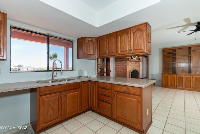 kitchen with kitchen peninsula, a brick fireplace, ceiling fan, sink, and light tile patterned flooring