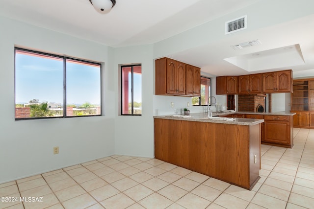 kitchen with light stone countertops, kitchen peninsula, sink, and light tile patterned floors