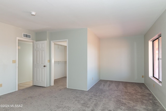 unfurnished bedroom featuring a walk in closet, light carpet, and a closet