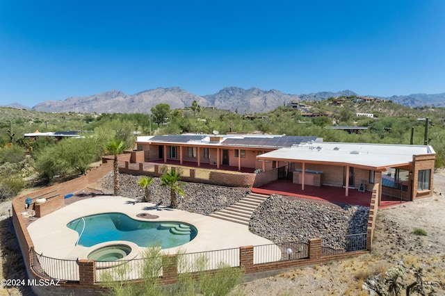 rear view of house with a mountain view, a swimming pool with hot tub, a patio, and solar panels