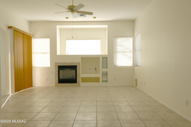 unfurnished living room featuring ceiling fan, plenty of natural light, a tile fireplace, and light tile patterned flooring