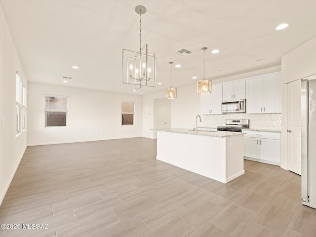 kitchen with pendant lighting, sink, appliances with stainless steel finishes, white cabinets, and a center island with sink