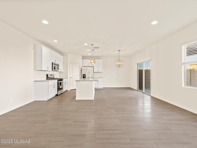 kitchen featuring white cabinetry, a chandelier, hanging light fixtures, stainless steel appliances, and a center island with sink