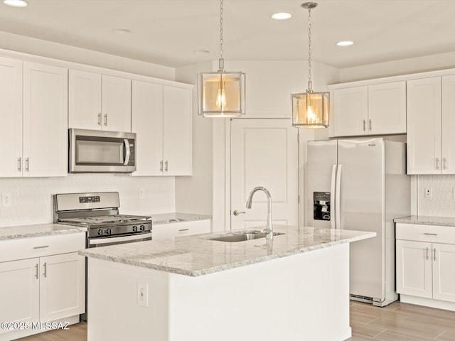 kitchen featuring white cabinetry, appliances with stainless steel finishes, decorative light fixtures, and a center island with sink