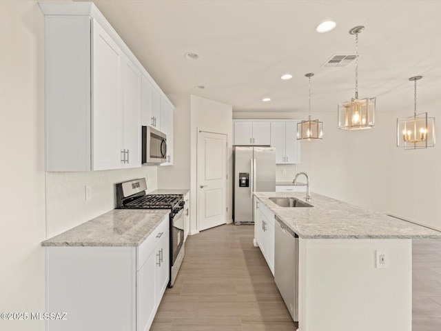 kitchen featuring sink, white cabinetry, appliances with stainless steel finishes, pendant lighting, and a kitchen island with sink