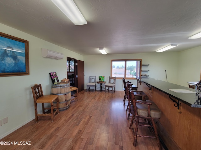 dining room featuring a wall mounted air conditioner, wood-type flooring, and a textured ceiling