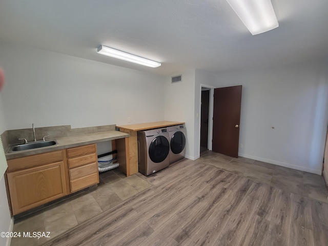 clothes washing area with sink, light hardwood / wood-style flooring, and washing machine and clothes dryer