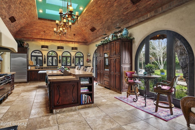 kitchen with stainless steel fridge, dark brown cabinets, an inviting chandelier, and brick ceiling