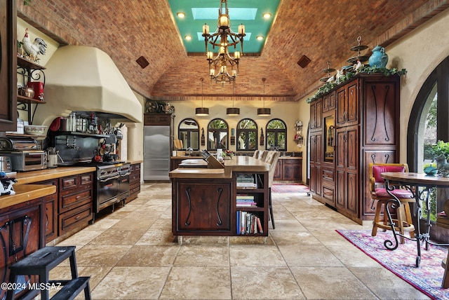 kitchen with premium appliances, an island with sink, a chandelier, vaulted ceiling, and brick ceiling