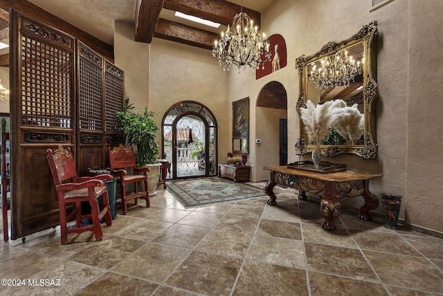 entrance foyer with a towering ceiling, beamed ceiling, and a notable chandelier