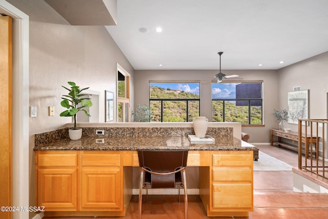 kitchen featuring dark stone countertops, a healthy amount of sunlight, ceiling fan, and built in desk