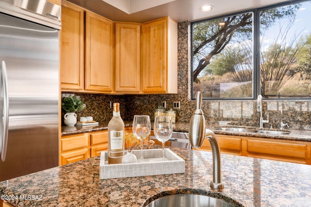 kitchen featuring tasteful backsplash, stainless steel built in fridge, dark stone countertops, and sink