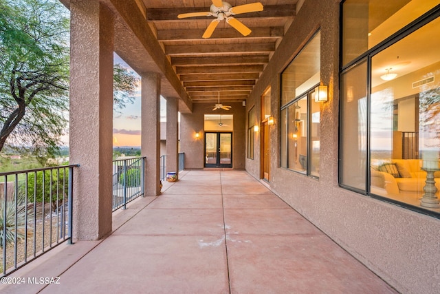 patio terrace at dusk featuring ceiling fan and a balcony