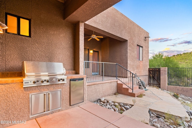 patio terrace at dusk with a grill, ceiling fan, and exterior kitchen