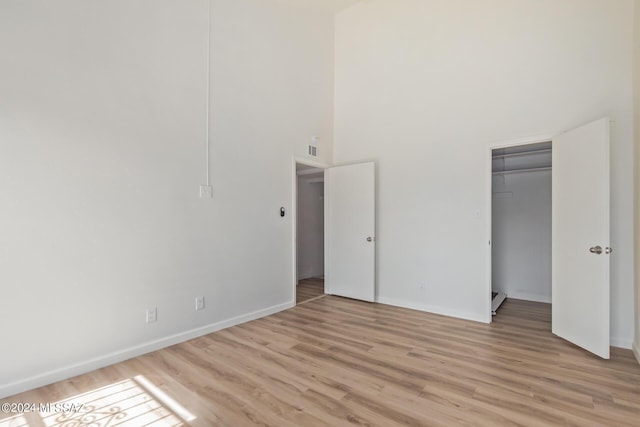 unfurnished bedroom featuring a high ceiling, light hardwood / wood-style floors, and a closet