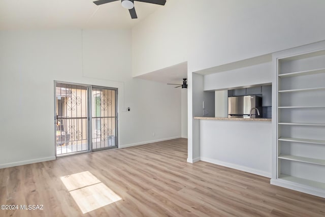 unfurnished living room with built in shelves, ceiling fan, light hardwood / wood-style floors, and a high ceiling