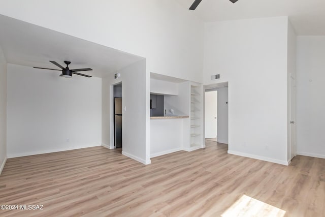 unfurnished living room with built in shelves, light hardwood / wood-style floors, ceiling fan, and a high ceiling