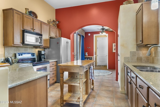 kitchen featuring ceiling fan, sink, stainless steel appliances, light stone counters, and backsplash