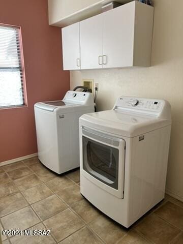 washroom featuring washing machine and clothes dryer, light tile patterned floors, and cabinets