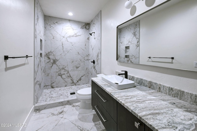 bathroom with toilet, a tile shower, and vanity