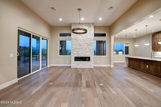 unfurnished living room featuring sink, a high ceiling, a fireplace, and light wood-type flooring