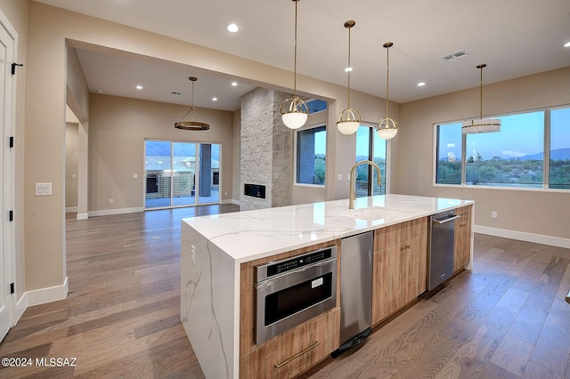 kitchen featuring sink, hanging light fixtures, a large island with sink, and light stone counters