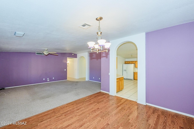 unfurnished room with a textured ceiling, light hardwood / wood-style floors, and ceiling fan with notable chandelier