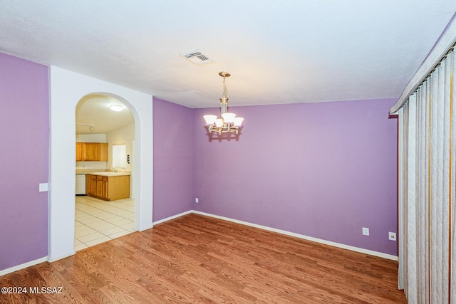 spare room with light hardwood / wood-style flooring, a chandelier, and sink