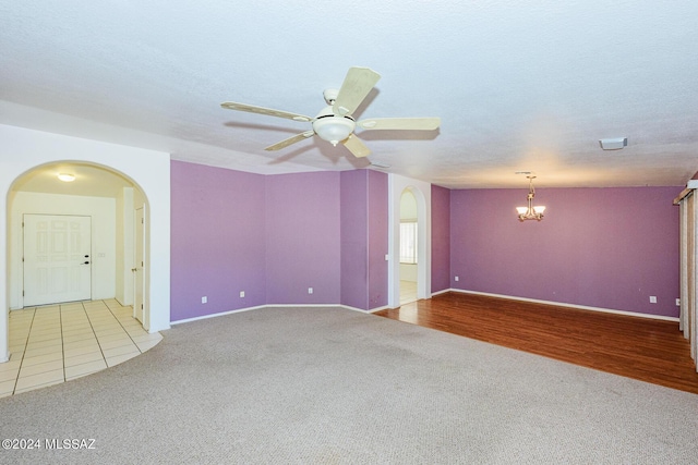 unfurnished room featuring a textured ceiling, ceiling fan with notable chandelier, and light colored carpet