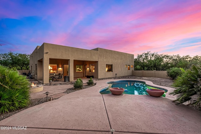 pool at dusk with an outdoor fire pit and a patio