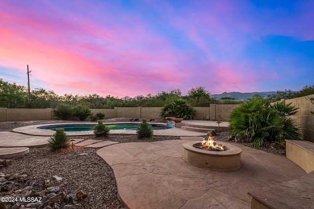 patio terrace at dusk featuring a fenced in pool, a fenced backyard, and a fire pit