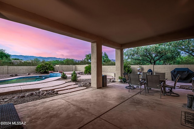 patio terrace at dusk with a mountain view, outdoor dining area, a fenced backyard, and a fenced in pool