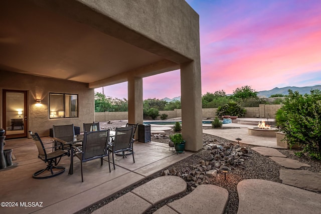 patio terrace at dusk with a fenced backyard, a mountain view, a fire pit, a fenced in pool, and outdoor dining space