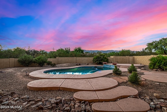 pool at dusk with a patio area, a fenced backyard, and a fenced in pool