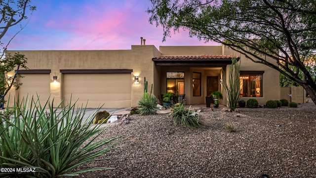 southwest-style home with a tile roof, driveway, an attached garage, and stucco siding