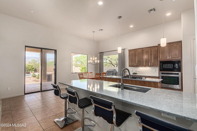 kitchen featuring sink, light tile patterned floors, black microwave, light stone counters, and stainless steel oven