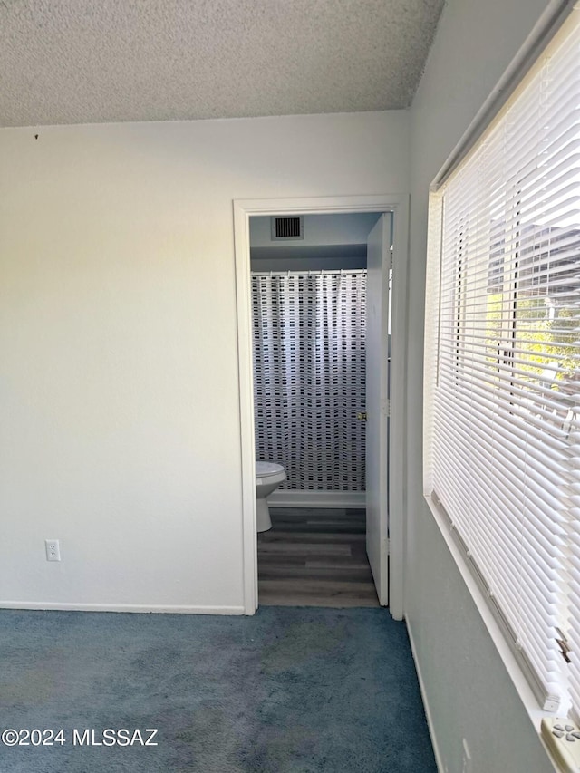 hall featuring a textured ceiling and dark colored carpet