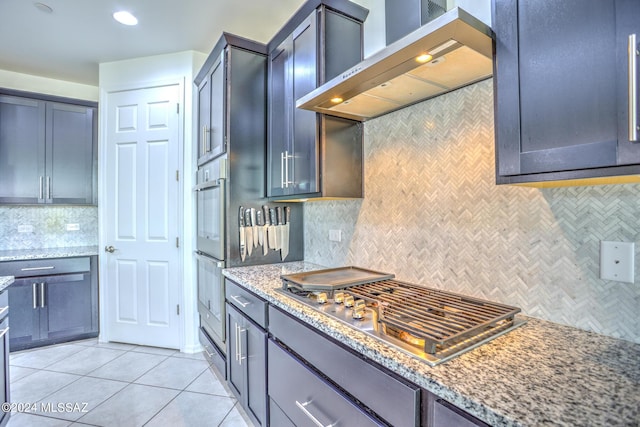 kitchen with light tile patterned floors, stainless steel appliances, light stone countertops, decorative backsplash, and wall chimney exhaust hood