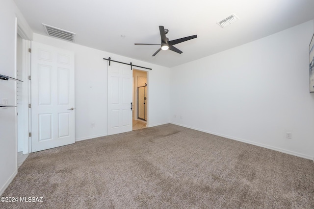 unfurnished bedroom featuring light carpet, a barn door, and ceiling fan