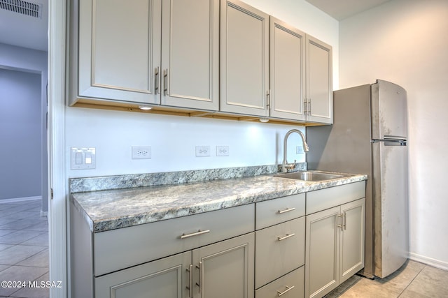 kitchen with light tile patterned flooring, gray cabinetry, sink, and stainless steel refrigerator