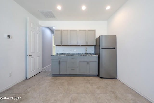 kitchen with sink, gray cabinets, light stone countertops, and stainless steel refrigerator