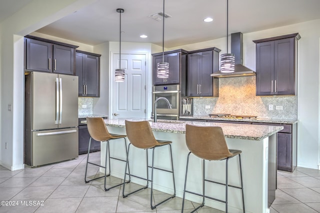 kitchen with pendant lighting, stainless steel appliances, a center island with sink, and wall chimney range hood